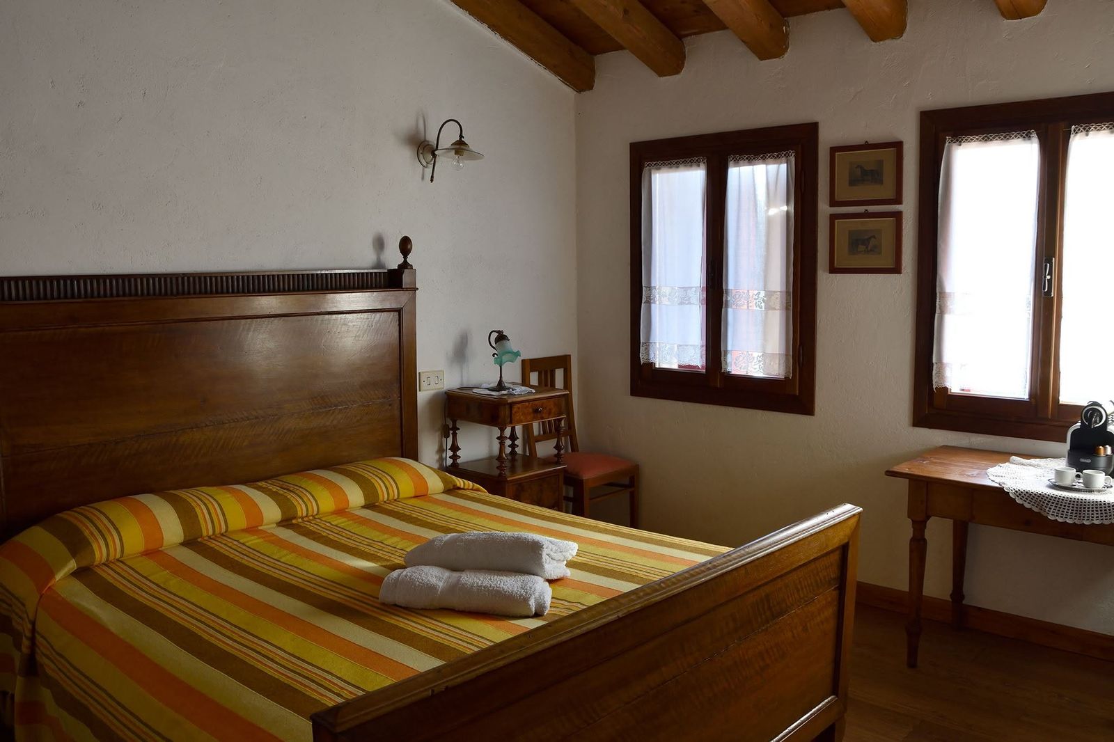 Camera con letto in legno, coperta a righe arancio e due finestre sul giardino