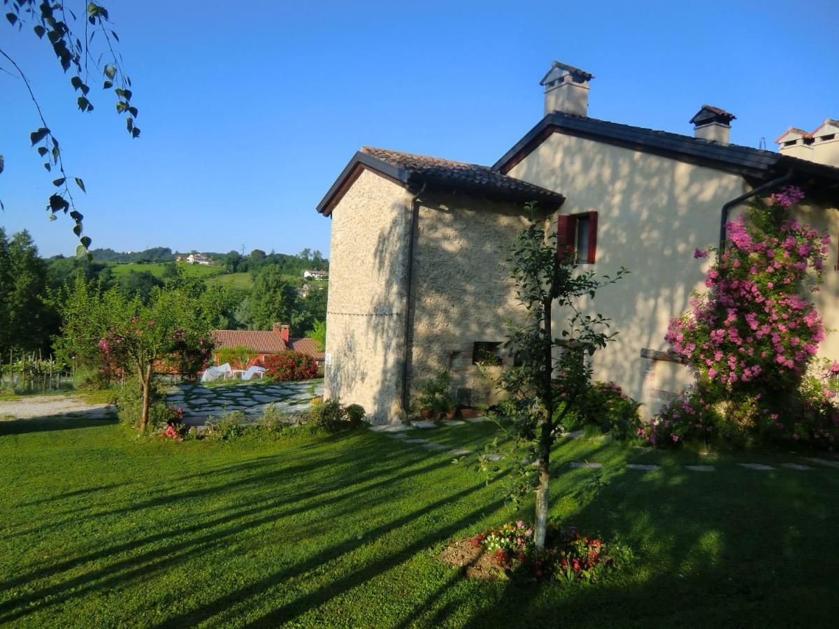 Il lato in pietra della casa, con le rose rampicanti e il prato all'ombra